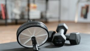 Ab roller and dumbbells on yoga mat, perfect for a home workout routine and healthy lifestyle.