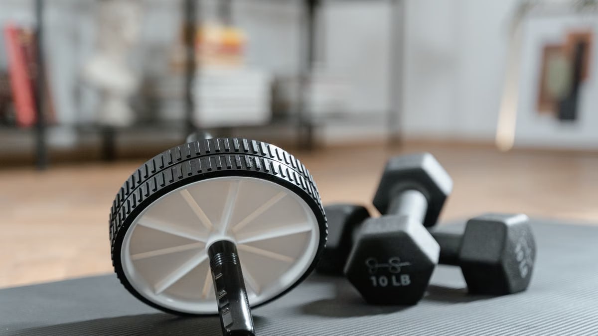 Ab roller and dumbbells on yoga mat, perfect for a home workout routine and healthy lifestyle.